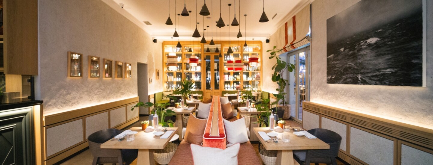 Hell ausgeleuchteter Innenraum des Restaurants Beetle von Feinkost Käfer in München mit Holztischen und einer Sitzbank im Mittelpunkt.