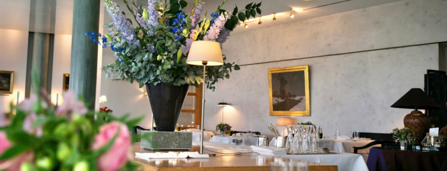 Innenraum des Restaurants Wielandshöhe mit einem Holztisch, weiß eingedeckten Tischen und Blumendeko.