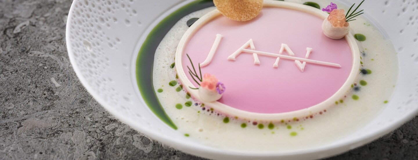 Eine kunstvoll angerichtete Speise in Pastelltönen mit dem Schriftzug JAN auf einem weißen Teller.