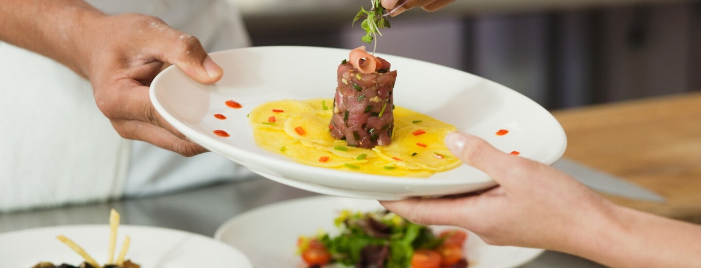 Ein Koch garniert ein Gericht mit Thunfischtartar auf einem weißen Teller in einer Restaurantküche.
