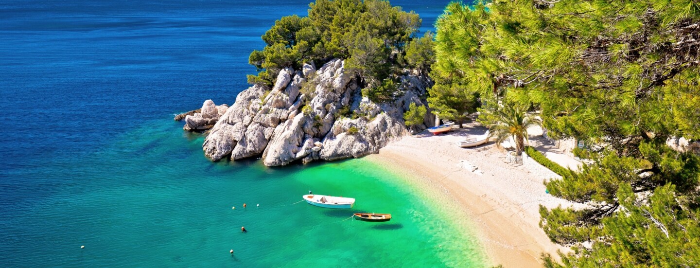 Kleine Sandbucht mit Fischerbooten im türkisblauen Meer, umgeben von Felsen und Kiefernwald.