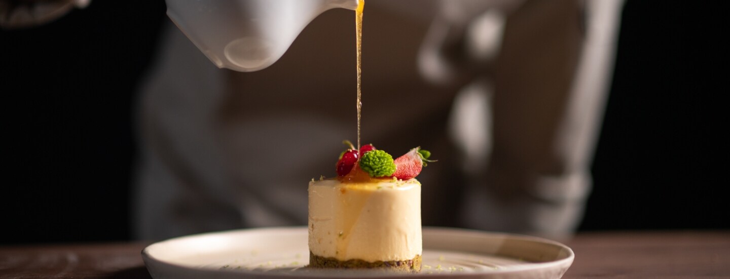 Ein Koch gießt Soße über einen kleinen runden Kuchen auf einem großen Teller.