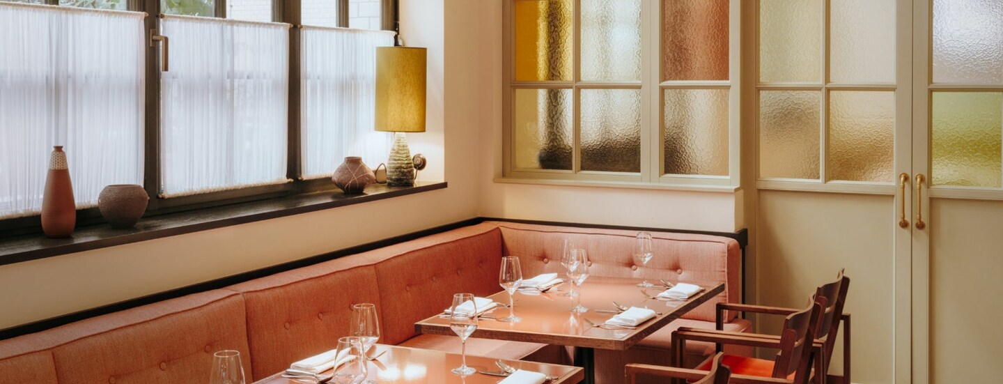 Interieur mit gedeckten Tischen und korallfarbenen Sitzmöbeln am Fenster.