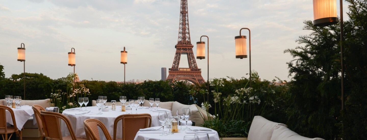 Dachterrasse eines Restaurants mit weiß eingedeckten Tischen vor dem Eiffelturm.