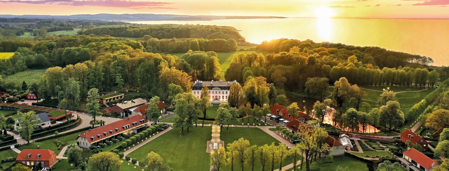 Luxuriöses Hotelresort mit Park- und Waldlandschaft an Meeresküste bei Sonnenuntergang.