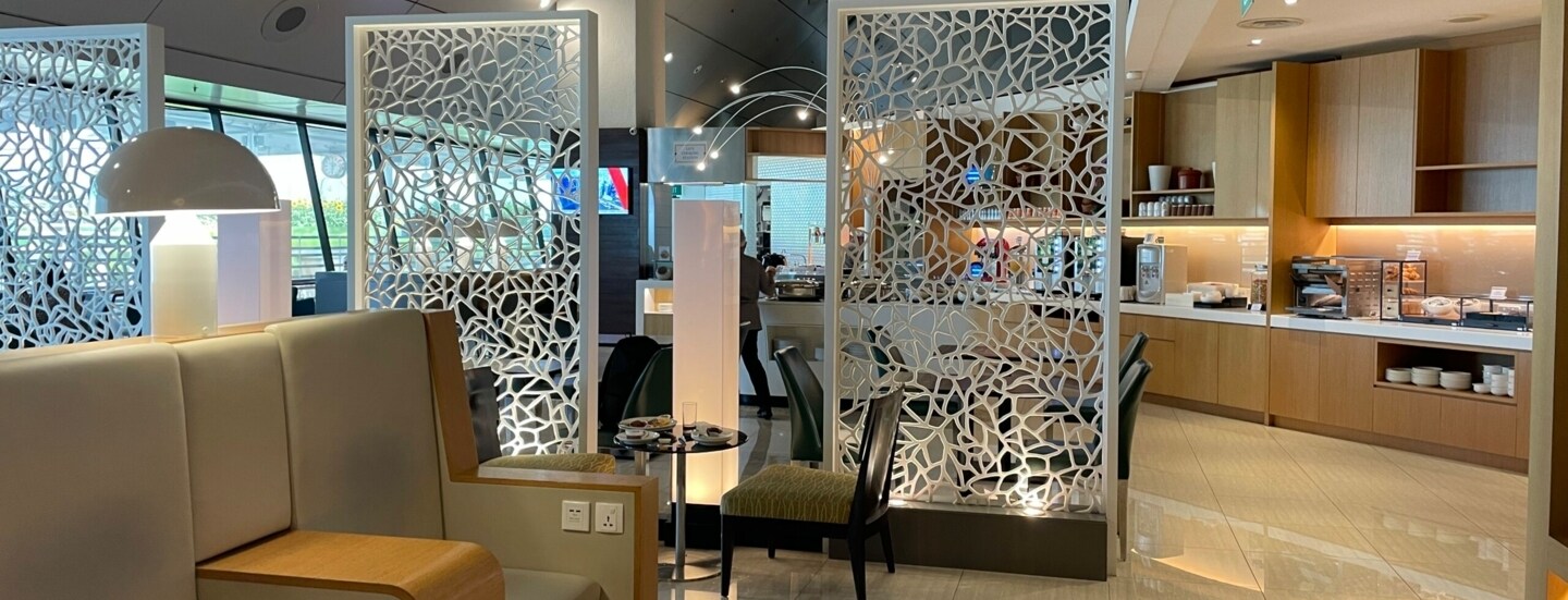 Einblick in eine hell eingerichtete Ambassador Lounge mit zwei Ledersesseln im Vordergrund, dahinter, durch Trennwände abgegrenzter Büffetbereich.