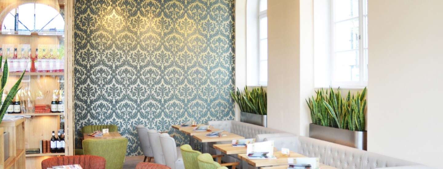 Heller Innenraum des ALEX Restaurants in Düsseldorf mit verschieden farbigen Sofas und Stühlen und hellen Holztischen.