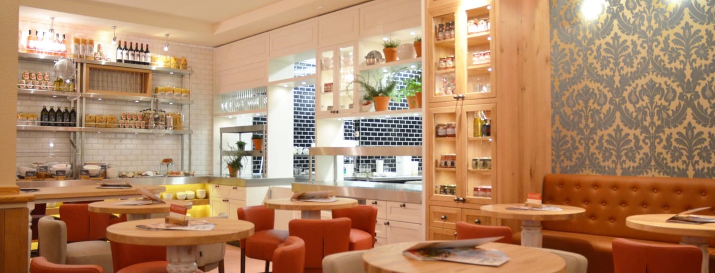 Innenraum des Restaurants ALEX Zwickau mit verschieden farbigen Stühlen und hellen Holztischen.