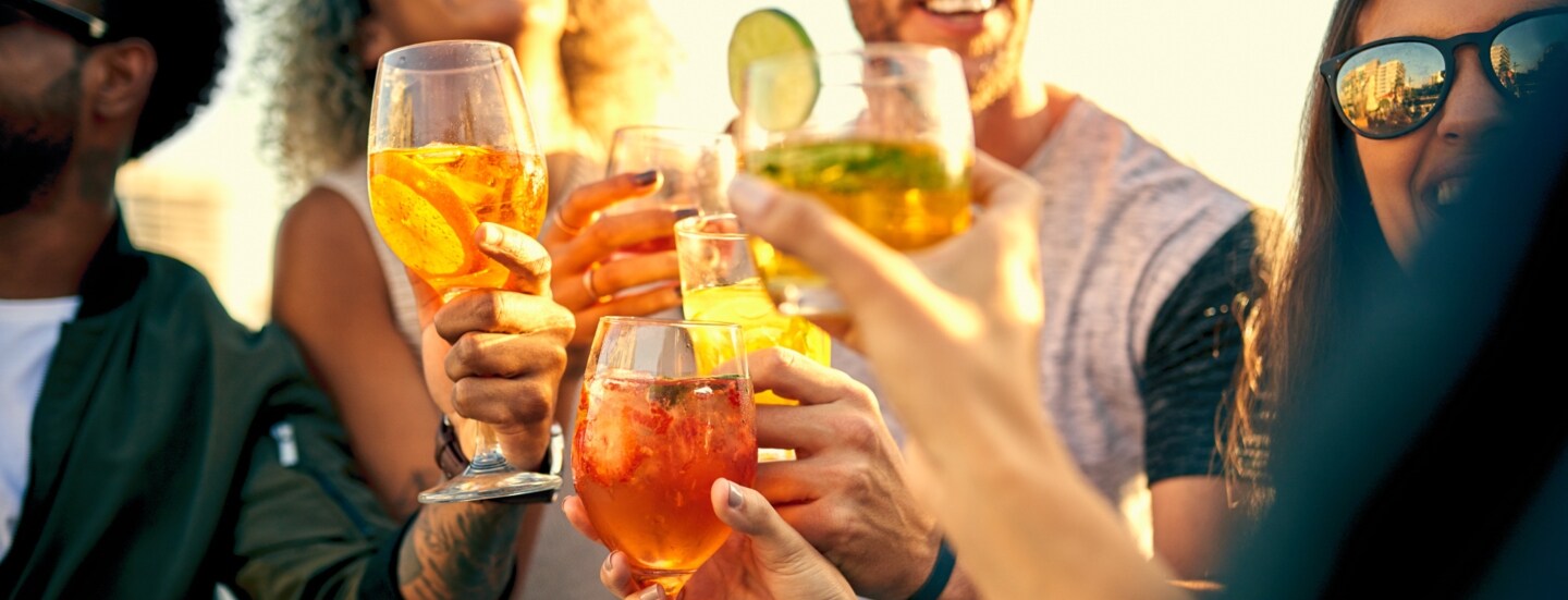 Vier gut gelaunte Personen mit Sonnenbrillen stoßen mit Cocktails an.