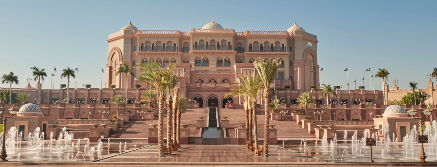 Außenansicht des Emirates Palace Mandarin Oriental Hotels in Abu Dhabi mit Palmen und Brunnen im Vordergrund.