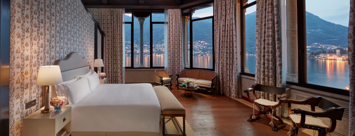 Großes, nobles Hotelzimmer mit Holzdecke, Blumentapete und Panoramablick auf den Comer See bei Abenddämmerung.