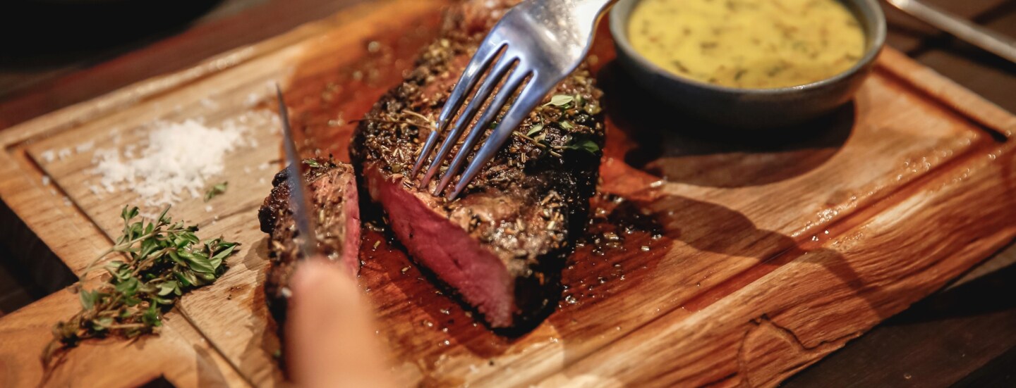 Nahaufnahme eines angeschnittenen Steaks auf einem Holzbrett neben einer Schale mit Soße.