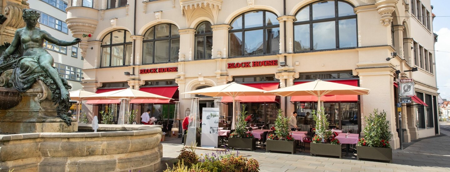 Block House Restaurant mit Außengastronomie in einem historischen Gebäude an einem Platz mit Brunnen in einer Altstadt.