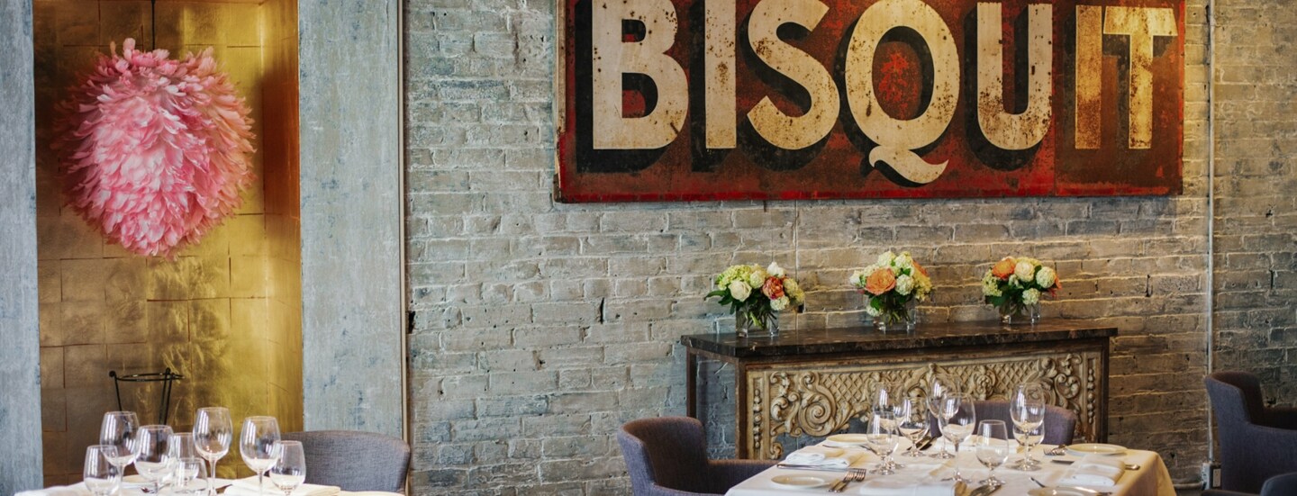 Weiß eingedeckte Restauranttische in einem Raum mit Backsteinwand und antikem Werbeplakat.