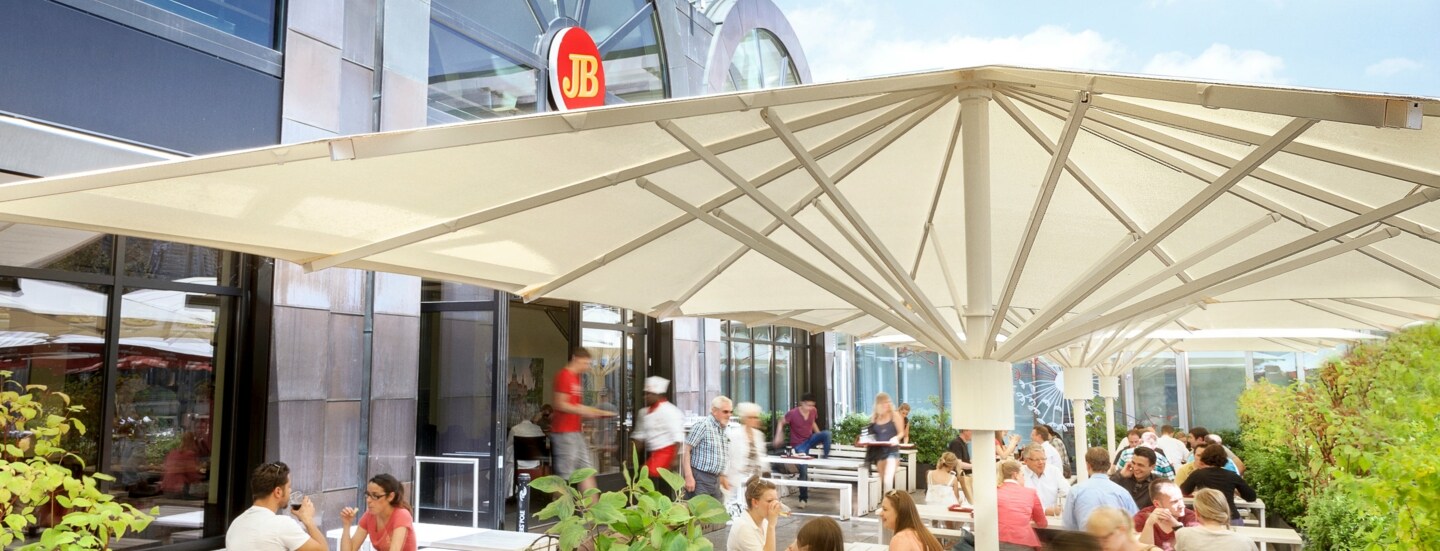 Außengastronomie auf einer Terrasse an einer Jim Block Filiale mit moderner Glasfassade.