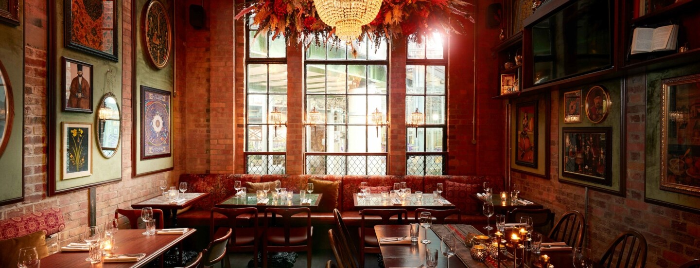 Eingedeckte Holztische auf einem Perserteppich im Speisesaal eines orientalischen Restaurants mit Backsteinwänden und warmer Beleuchtung.