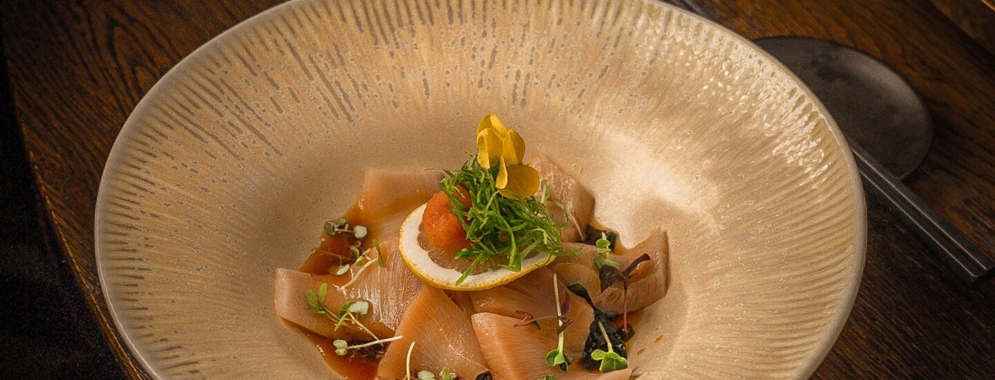 Ein heller Teller mit garnierten asiatischen Teigtaschen auf einem Holztisch.