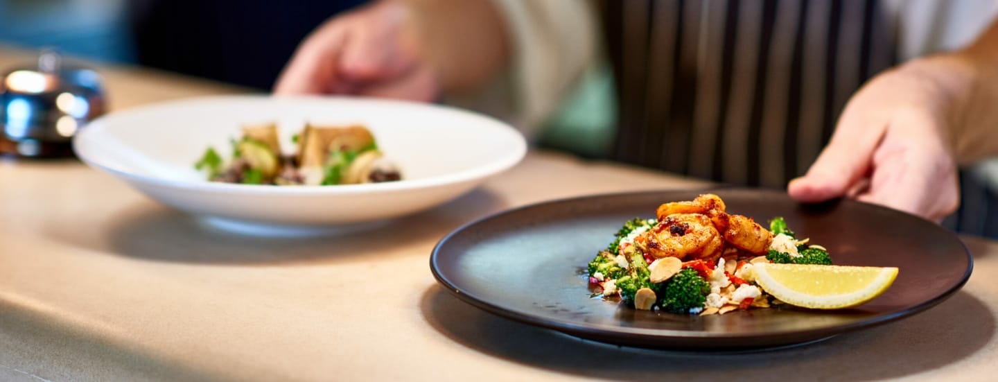 Ein Koch stellt zwei Teller mit zubereiteten Speisen auf die Theke.