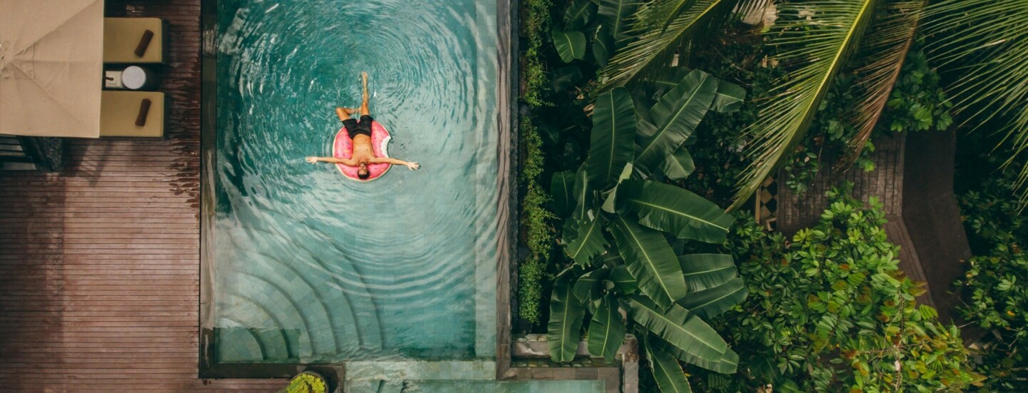 Junger Mann auf einer Luftmatratze in einem Infinity-Pool mit tropischer Umgebung.