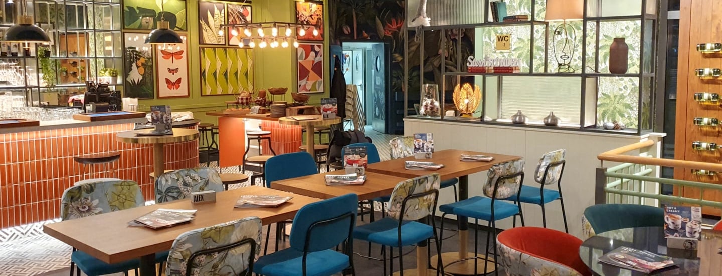 Innenansicht des ALEX in Ludwigshafen, mit Holztischen, bunten Stühlen und dekorativen Bildern an der Wand.