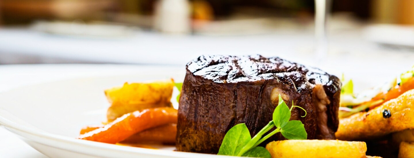 Gegrilltes Rinderfilet auf weißem Teller mit gebratenen Karotten und grünen Erbsensprossen.