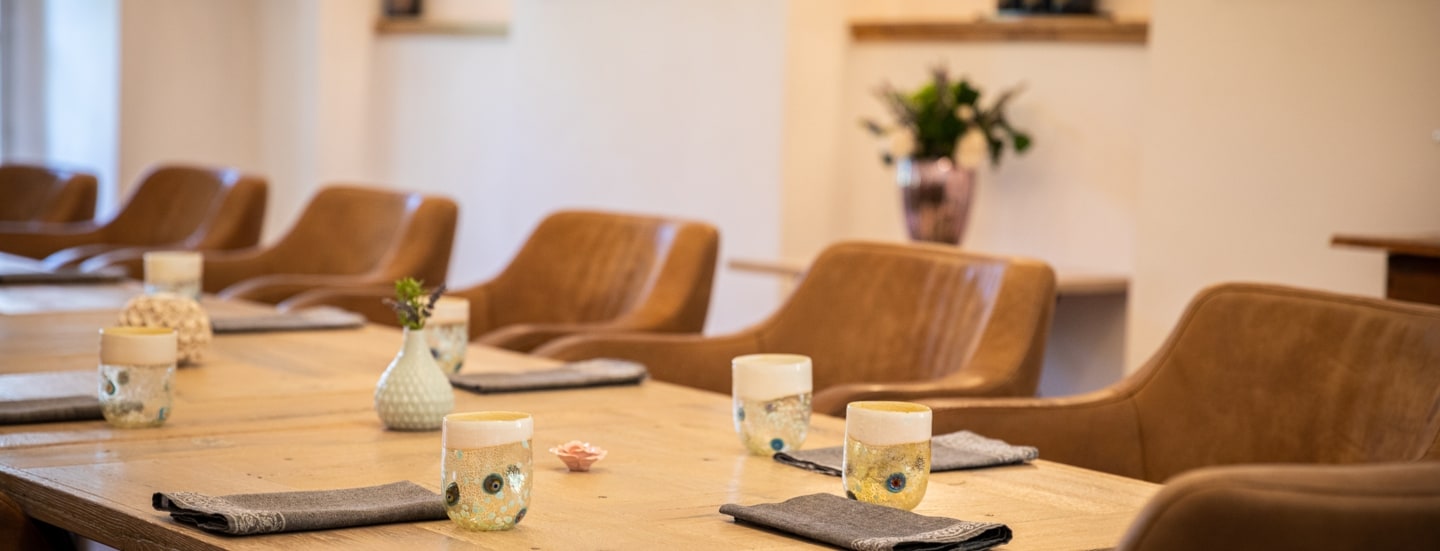 Gedeckte Holztische an denen cognacfarbenen Ledersessel stehen eines Sternerestaurants, im Hintergrund stehen Champagnerflaschen auf Regalen.