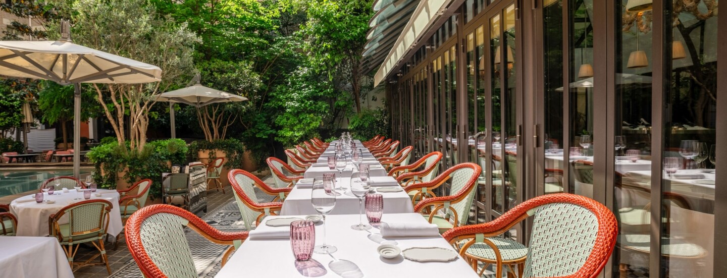 Begrünter Innenhof eines eleganten Restaurants mit gedeckten Tischen und Sonnenschirmen.