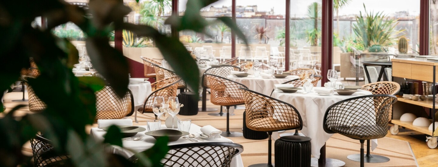 Interieur-Aufnahme eines modernen Restaurants mit gedeckten Tischen und bodentiefen Fenstern, die den Blick auf Paris freigeben.