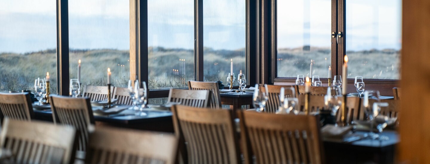 Gastraum der Sylter Sansibar, mit eleganten Tischen und Stühlen aus dunklem Holz und einem herrlichen Ausblick auf die umliegende Dünenlandschaft.
