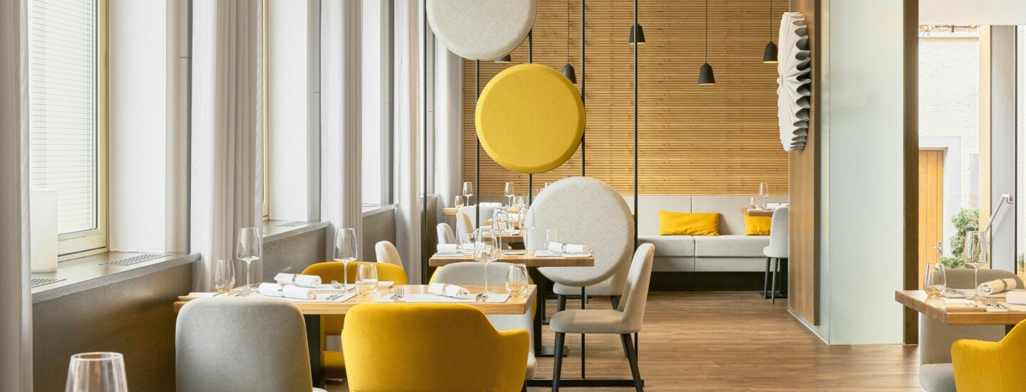 Helles stilvolles Interieur mit gelben und cremefarbenen Sitzmöbeln, dekorativer Trennwand und holzverkleideten Wänden.