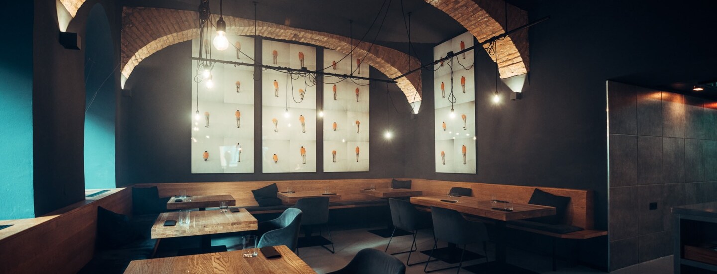 Moderner Speisesaal mit eingedeckten Holztischen und dunklen Wänden mit Gewölbedecke.