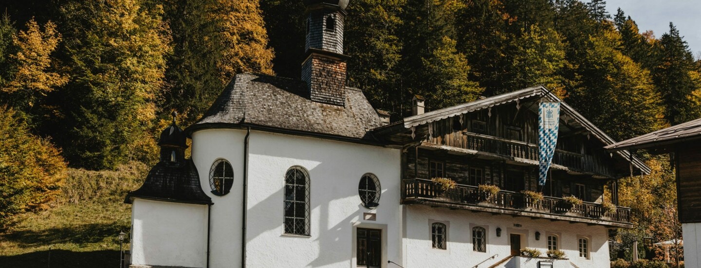 Traditionelles, bayerisches Gasthaus mit Kapelle vor einem Waldgebiet.