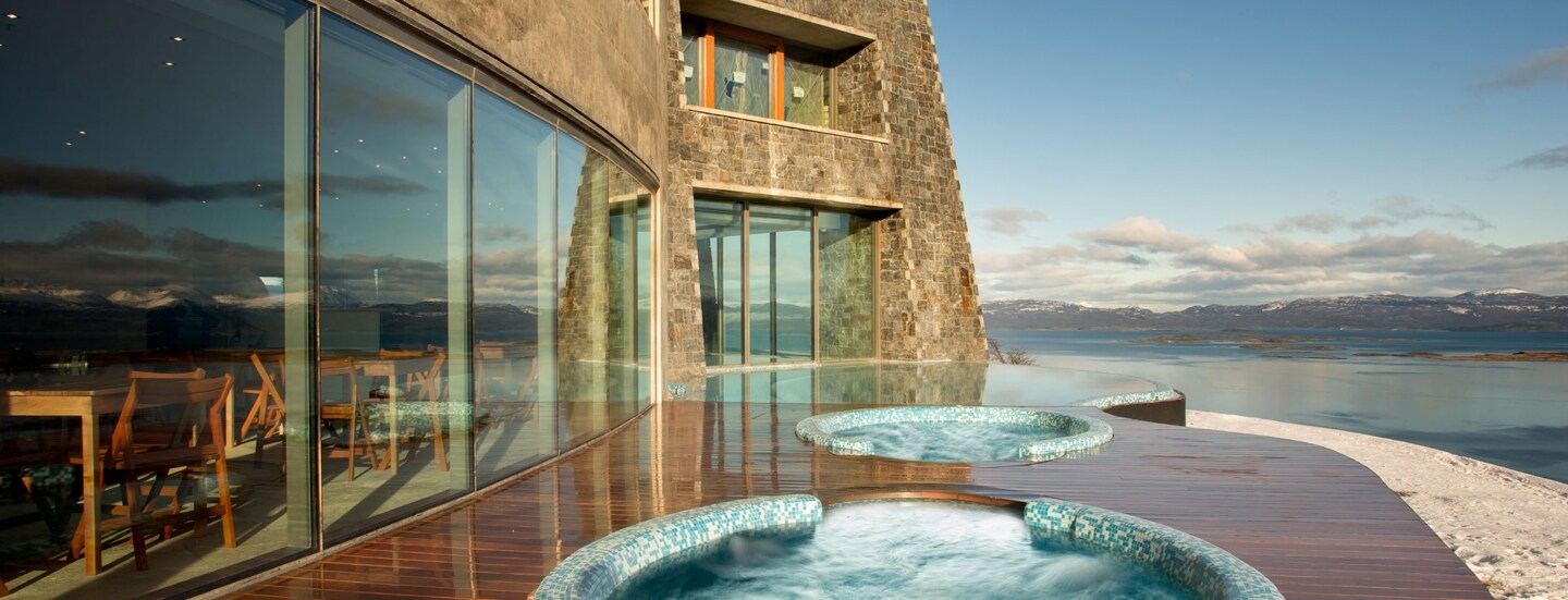 Jacuzzis auf einer Hotelterrasse mit Blick auf eine Schneelandschaft am Wasser.