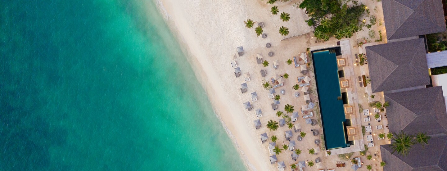 Hotelresort mit Pool und Sanstrand am türkisblauen Meer aus der Vogelperspektive.