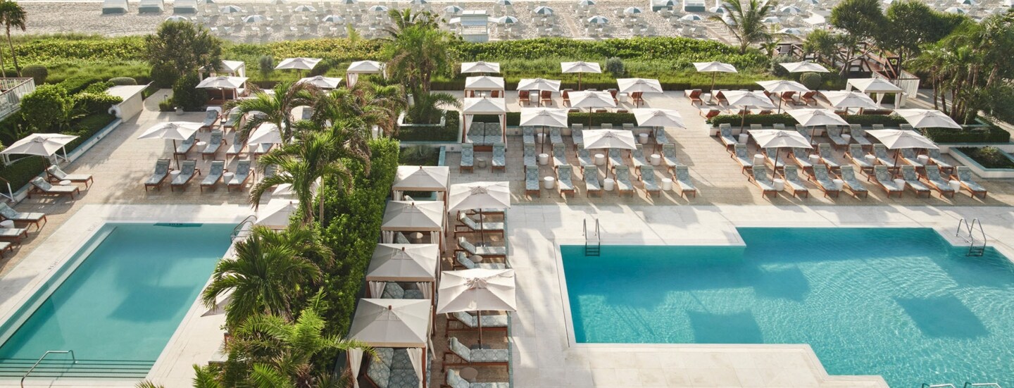 Hotelterrasse mit Palmen und Liegen am Pool an einem weißen Sandstrand mit weiteren Liegen.