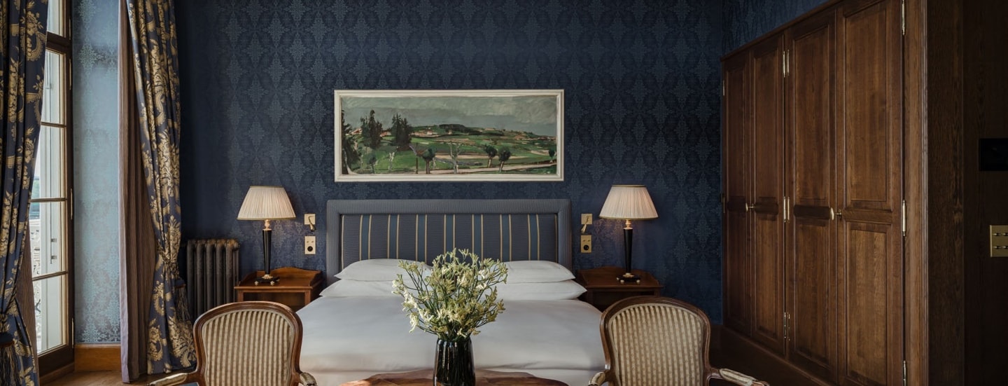 Gemütliches Hotelzimmer mit Doppelbett vor dunkelblauer Tapete und großem Holzkleiderschrank.