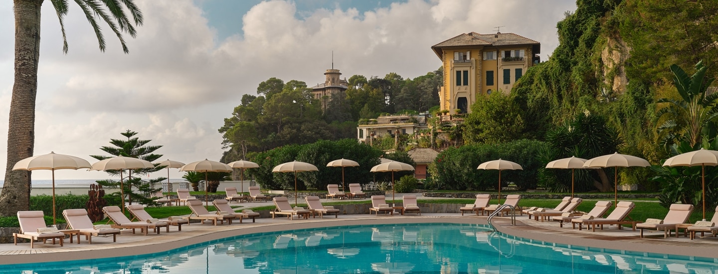 Luxuriöse Hotelterrasse mit Pool und Liegestühlen an einer mediterranen Küste.