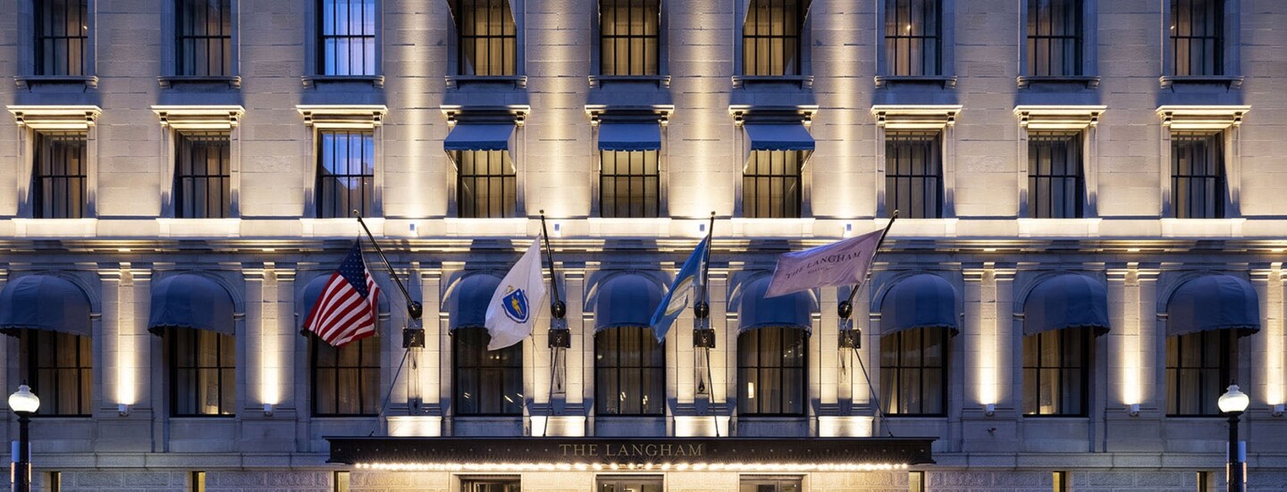 Beleuchtete Fassade eines Luxushotels mit wehenden Fahnen über dem Eingangsbereich.