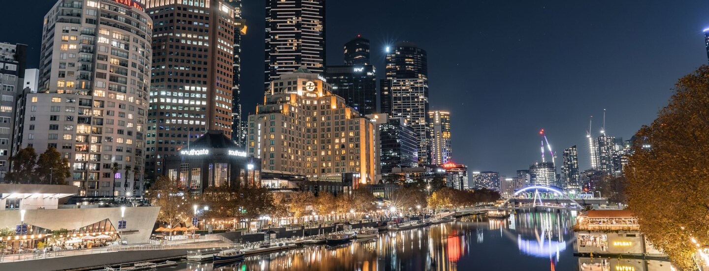 Beleuchtete Skyline mit Hochhäusern an einem Flussufer bei Nacht.