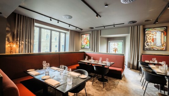 Blick in das Innere eines Restaurants mit eingedeckten Tischen und roten Sitzbänken.