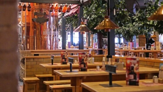 Gastronomiebereich in einem Brauhaus mit Holztischen und großem Kupferkessel.