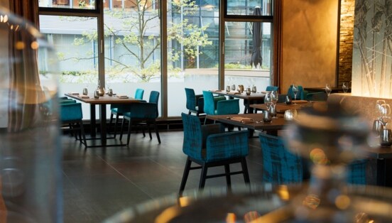 Blaue Polsterstühle an eingedeckten Tischen im Speisesaal eines Restaurants mit bodentiefen Fenstern.