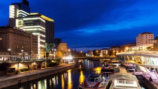 Moderner Hotelkomplex am Donaukanal mit Barkassen in Wien bei Nacht.