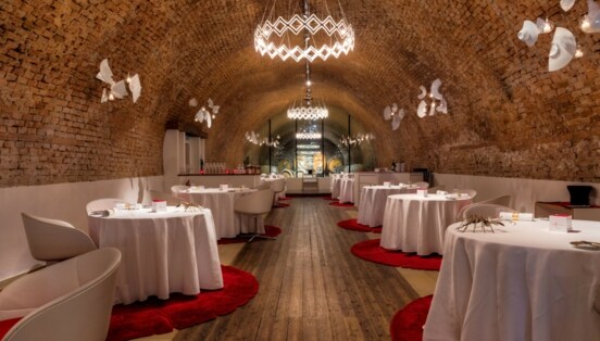 Speisesaal mit weiß eingedeckten, runden Tischen in einem Ziegelgewölbekeller.
