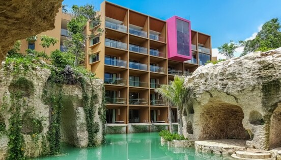 Moderner Hotelkomplex, umgeben von bepflanzten Felsen an einem Pool mit türkisfarbenem Wasser.