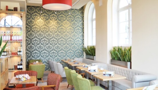Heller Innenraum des ALEX Restaurants in Düsseldorf mit verschieden farbigen Sofas und Stühlen und hellen Holztischen.