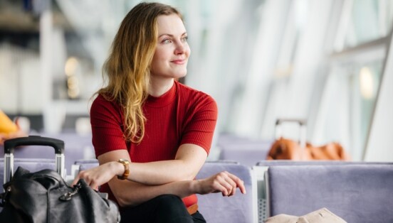 Eine Frau sitzt lächelnd im Wartebereich in einem Flughafenterminal.