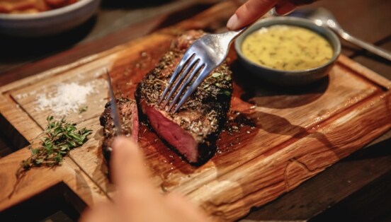 Nahaufnahme eines angeschnittenen Steaks auf einem Holzbrett neben einer Schale mit Soße.