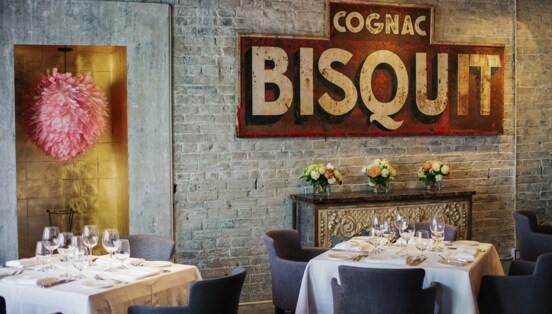 Weiß eingedeckte Restauranttische in einem Raum mit Backsteinwand und antikem Werbeplakat.