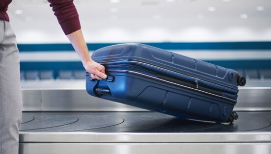 Eine Person nimmt einen blauen Hartschalenkoffer von einem Gepäckband.
